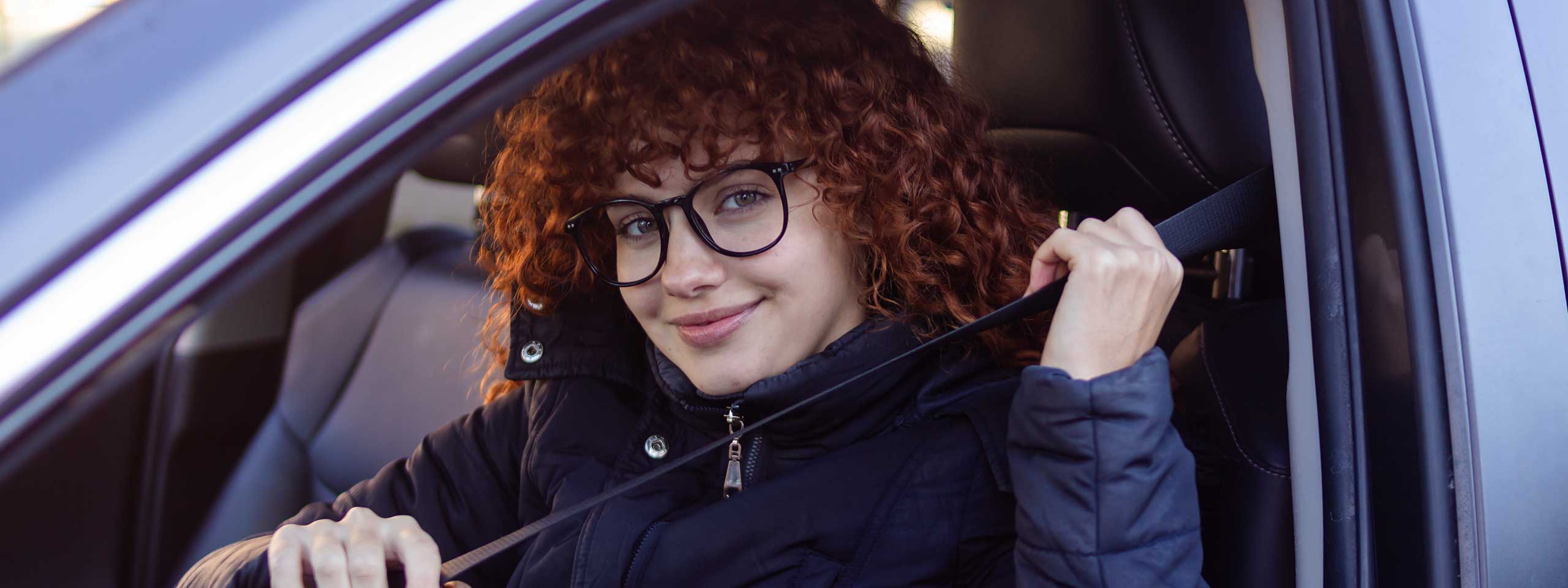 Frau mit Brille schnallt sich im Auto an